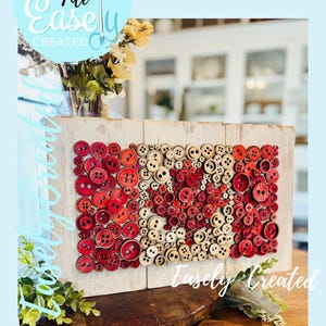 May include: A wooden sign decorated with red and cream-colored buttons. The buttons are arranged in a pattern, with the text "Easely Created" and "Digital Cut File" visible. The sign is displayed on a wooden surface.