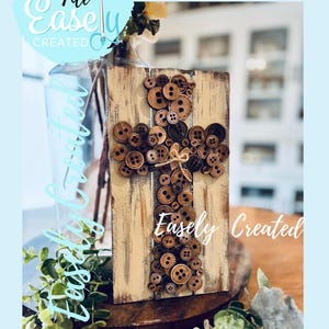 Puede incluir: Cruz de madera decorada con botones marrones de varios tamaños. La cruz está montada sobre una tabla de madera envejecida de color crema. Las palabras "Easely Created" están escritas en la cruz. Las palabras "Digital Cut File" están escritas arriba.