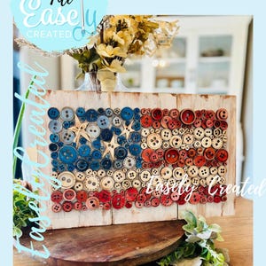 May include: A wooden plaque featuring a patriotic design made of buttons. The artwork depicts the American flag, with red, white, and blue buttons arranged to form the stars and stripes. The text "Digital Cut File Easily Created" is in the image.