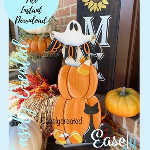 May include: A wooden Halloween decoration featuring a stack of three pumpkins with a ghost holding a "BOO" banner on top. The bottom pumpkin has a black cat silhouette. The decoration is on a black base with candy corn and the text "Easly Created".