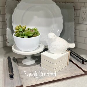 May include: A white ceramic bird figurine sits on a stack of white boxes on a wooden tray with a gray and white geometric pattern. A white ceramic planter with a succulent plant sits on a white pedestal on the tray. The tray has a black metal handle. The text "EaslyCreated" is printed on the tray.