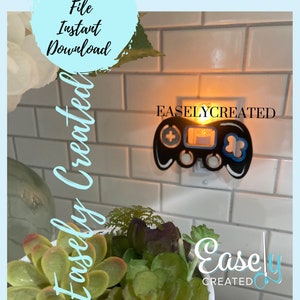 May include: A black and blue nightlight shaped like a video game controller plugged into an electrical outlet. The nightlight is lit and the text "EASELYCREATED" is visible above the nightlight.