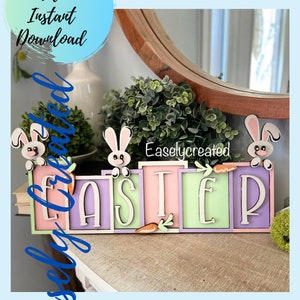 May include: A pastel-colored Easter sign with the word "EASTER" spelled out in individual letter blocks. Each block is a different color: pink, lavender, green, and white. Bunny figures and carrots decorate the sign.