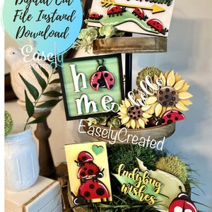 Könnte beinhalten: Ein dreistufiges Tablett, das mit Marienkäfer-Motiven aus Holz verziert ist. Die Schilder sagen "Ladybug Crossing", "Home", "Hello", "Ladybug Wishes".