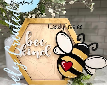 Puede incluir: Un letrero hexagonal de madera con una abeille y las palabras "bee kind" en letras blancas. El letrero tiene un patrón de panal y un corazón rojo. El letrero está sobre una superficie blanca con plantas verdes.