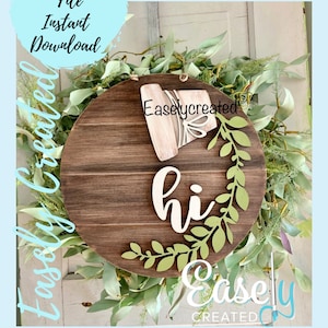 May include: A wooden round sign with the word "hi" in white script with green leafy vines around it. The sign is surrounded by a green leafy wreath. The text "Easlycreated" is visible on the sign.