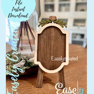 Peut inclure: Une pancarte en bois avec un fond brun et un cadre blanc. La pancarte est ornée d'un motif de feuilles vertes décoratives en haut et est posée sur un petit chevalet en bois. La pancarte porte l'inscription "Easlycreated" en bas.