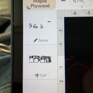 以下が含まれることがあります： コンピューター画面に、歯の列の白黒画像が表示されたデザインソフトウェアのインターフェースが表示されています。ソフトウェアには、「スコア」と「カット」のオプションと、インチ単位の目盛りが付いた定規があります。画面の上部には、「メープル合板」と「67％」のテキストが表示されています。