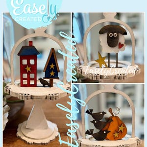 May include: Wooden laser-cut decorative pieces. The image shows a red and blue house, a blue and gold tree, a black bird, a sheep with a red heart, a gold star, a pumpkin with gold stars, and three black birds. The text "Digital Cut File Easely Created" is also visible.
