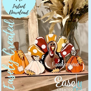 May include: A wooden turkey figurine with a red, yellow, and white polka dot tail. The turkey is surrounded by three wooden pumpkins, one of which is white. The pumpkins have painted leaves and a small patch on them. The turkey has a red heart on its chest and the words "Easlycreated" written on it. The background is a wooden surface.