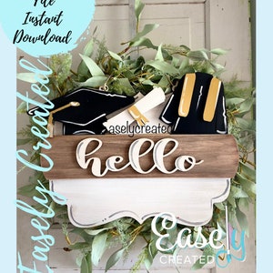 May include: A graduation wreath with a black graduation cap, a diploma, and a graduation gown. The wreath is decorated with green leaves and the words "hello" and "Easley Created" are on the wreath.
