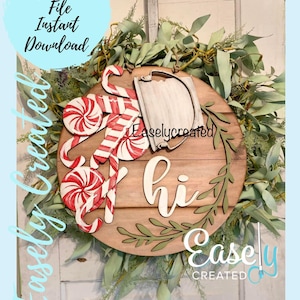 May include: A wooden round sign with the word "hi" in white script. The sign is decorated with a wreath of green leaves, candy canes, and a white sign with the text "Easlycreated".