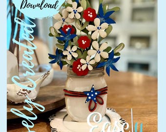 May include: A white mason jar with a red, white, and blue ribbon and a star on it. The jar is filled with a bouquet of red, white, and blue flowers. The flowers are made of wood and are painted in a patriotic theme. The jar is sitting on a white, decorative plate. The text "Easley Created" is visible on the plate.