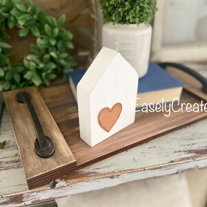 May include: A wooden tray with a black metal handle. The tray is decorated with a white wooden house with a brown heart cutout. The text "EaselyCreated" is visible on the tray.