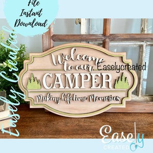 Puede incluir: Señal de madera con fondo marrón y borde verde. La señal dice "Bienvenido a nuestro CAMPER Haciendo recuerdos para toda la vida". Hay árboles verdes a cada lado de la palabra "CAMPER".