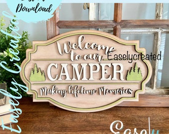 May include: Wooden sign with a brown background and a green border. The sign says "Welcome to our CAMPER Making lifetime memories". There are green trees on either side of the word "CAMPER".