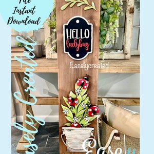 May include: A wooden sign with a green leafy branch, a black sign with the text "HELLO ladybug" and a green plant with red ladybugs in a white bucket. The sign is on a brown wooden background.