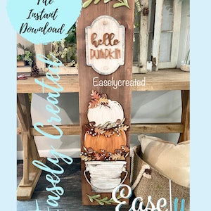Op de afbeelding: Een houten bord met een witte pompoen, een oranje pompoen en een witte emmer met een bruine rand. Het bord heeft ook een groen bladontwerp en een bord met de tekst "hello pumpkin".