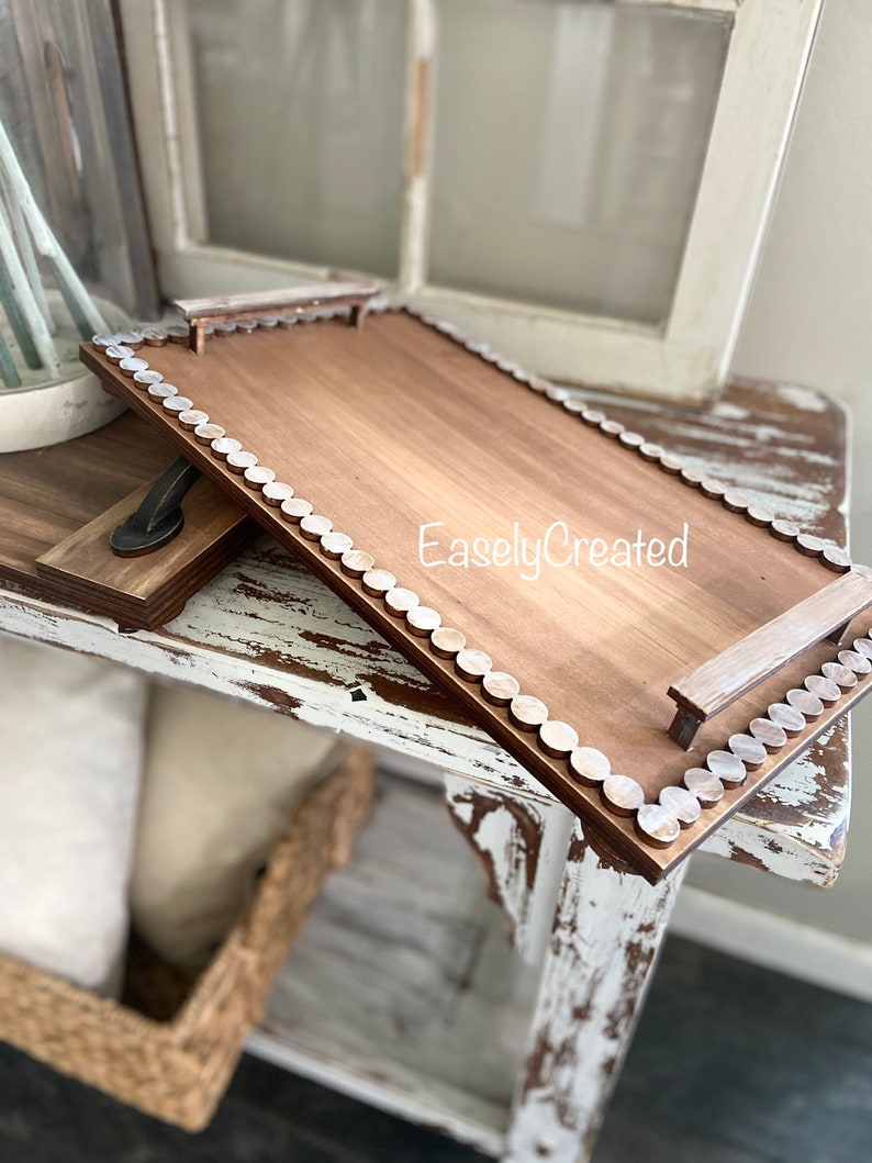 May include: A rectangular wooden tray with a brown stain and white painted edges. The tray has two wooden handles and a white bead border. The text "EaslyCreated" is printed on the tray.