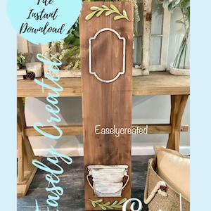 Op de afbeelding: Een bruin houten bord met een wit metalen frame, een witte metalen emmer en groene bladeren. Het bord zegt "Easlycreated".