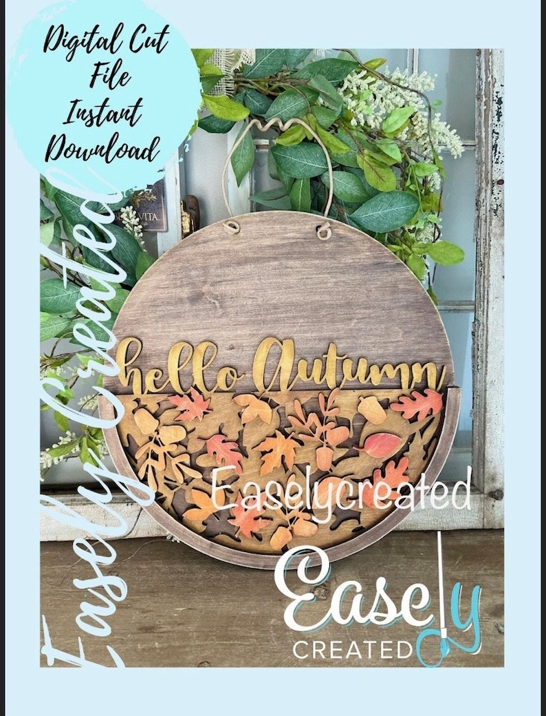 Pu&ograve; includere: Un cartello rotondo in legno con il testo "hello autumn" in lettere dorate. Il cartello &egrave; decorato con una cornice in legno marrone e un design ritagliato di foglie autunnali in arancio, rosso e giallo.