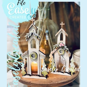 Puede incluir: Dos candelabros de madera con forma de iglesia y acabado blanco envejecido. Cada uno tiene una cruz en la parte superior y una abertura circular. Uno tiene una corona verde y el otro flores rosas. El texto "Digital Cut File Easely Created" es visible.
