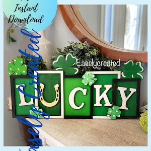 Könnte beinhalten: Ein Holzschild mit der Aufschrift "LUCKY" und einem Hufeisen in der Mitte. Die Buchstaben sind weiß mit schwarzen Umrandungen und auf grünem Hintergrund. Das Schild ist mit grünen Kleeblättern verziert.