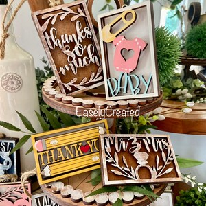 May include: A set of wooden signs with various sayings and designs. The signs are painted in different colours, including brown, white, yellow, and pink. The signs feature sayings like "Thanks so much", "Baby", "Thank You", and "Mr. & Mrs.".