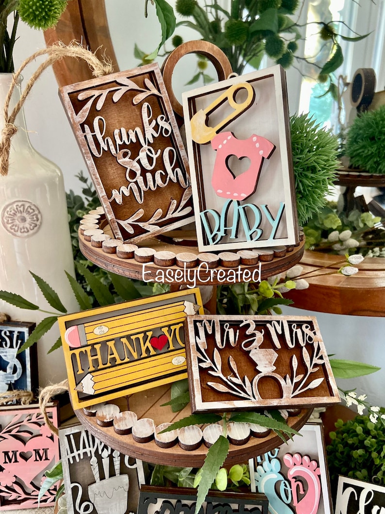 May include: A set of wooden signs with various sayings and designs. The signs are painted in different colours, including brown, white, yellow, and pink. The signs feature sayings like "Thanks so much", "Baby", "Thank You", and "Mr. & Mrs.".