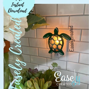 Könnte beinhalten: Ein grünes, schildkrötenförmiges Nachtlicht, das in eine Steckdose gesteckt ist. Das Licht ist an und beleuchtet den Panzer der Schildkröte. Die Schildkröte befindet sich an einer weißen gekachelten Wand. Der Text "Easley Created" ist auf dem Bild zu sehen.