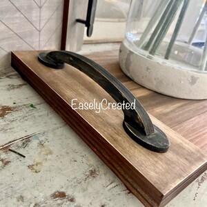 May include: A wooden serving tray with a black metal handle. The tray has a natural wood finish and the handle is distressed black. The text "EaslyCreated" is visible on the tray.