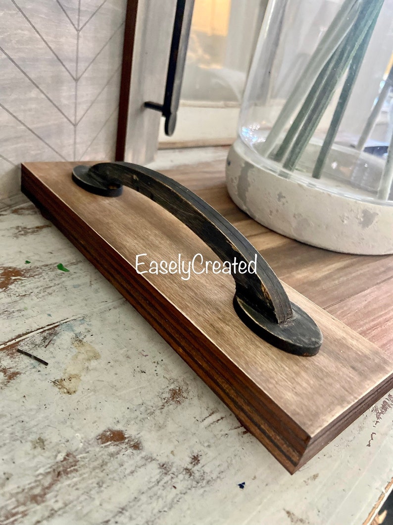 May include: A wooden serving tray with a black metal handle. The tray has a natural wood finish and the handle is distressed black. The text "EaslyCreated" is visible on the tray.