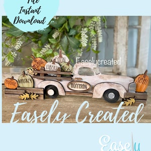 May include: A white wooden truck with a bed full of pumpkins. The pumpkins are decorated with names, including "Melanie", "Colin", "Liberty", "Whiskey", "Moonie", and "Hoffman". The truck is on a wooden surface with a sign that says "Easely Created".