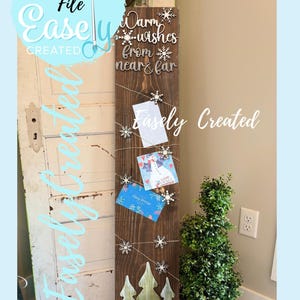 May include: A wooden sign with the text "Warm wishes from near & far" and "Easely Created". The sign features snowflakes, Christmas trees, and holds cards with string. The sign is a digital cut file.
