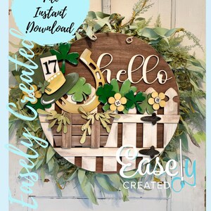 May include: A round wooden St. Patrick's Day wreath with a 'hello' sign, a leprechaun hat, shamrocks, and a horseshoe. The wreath has a white picket fence design and is surrounded by greenery. Text on the wreath says 'Easely Created' and 'Digital Cut File Instant Download'.