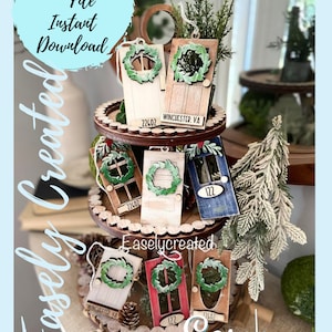 May include: A set of six wooden door ornaments with wreaths, each featuring a different colour and design. The ornaments are displayed on a tiered wooden stand with a rustic finish. The ornaments are labelled with the text "WINCHESTER, VA" and "22602".