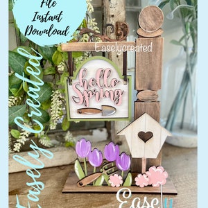 May include: A wooden sign with the text "Hello Spring" in pink letters, a birdhouse, and purple tulips. The sign is hanging from a wooden post with a heart-shaped cutout. The sign is surrounded by green leaves and flowers.