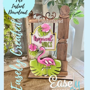 Puede incluir: Un letrero de madera con un flamenco rosa, hojas verdes y el texto "tropical vibes". El letrero está colgado de un arco de madera con el texto "Easlycreated" en él.