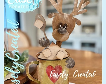 May include: A wooden reindeer-themed decoration with a mug design. The mug has a red heart and the text "Easely Created". The reindeer has antlers and is holding a spoon with marshmallows. The words "Digital Cut File" are in a blue circle.