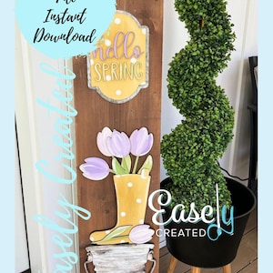 May include: A wooden sign with a yellow boot, purple tulips, and a white bucket. The sign also has a yellow sign that says "Hello Spring" with white polka dots. The sign is leaning against a black planter with a green bush.