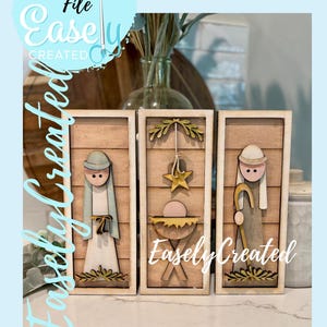 Op de afbeelding: Houten kerststal met drie panelen. Elk paneel toont een andere scène met figuren en decoratieve elementen. De tekst "Easely Created" is zichtbaar op de panelen en op de achtergrond. De woorden "Digital Cut File" zijn ook zichtbaar.