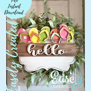 May include: A wooden wreath featuring a sign that reads "hello" and a row of colourful flip flops. The wreath is decorated with green leaves and the sign is on a brown wooden plank.
