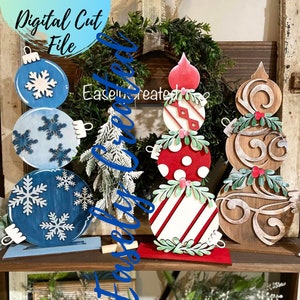 May include: Three wooden Christmas ornament decorations. The first ornament is blue with white snowflakes and is stacked on top of two other blue ornaments. The second ornament is red and white striped with a red polka dot ornament and a red and white diamond pattern ornament stacked on top. The third ornament is brown with a swirl pattern and has a green leafy sprig on top. The ornaments are on a wooden shelf.