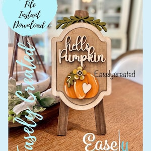 May include: Wooden sign with the text "hello Pumpkin" and a pumpkin illustration. The sign is on a wooden easel. The sign also has the text "Easelycreated" and "Ease Created". The image also has the text "Digital Cut File Instant Download".