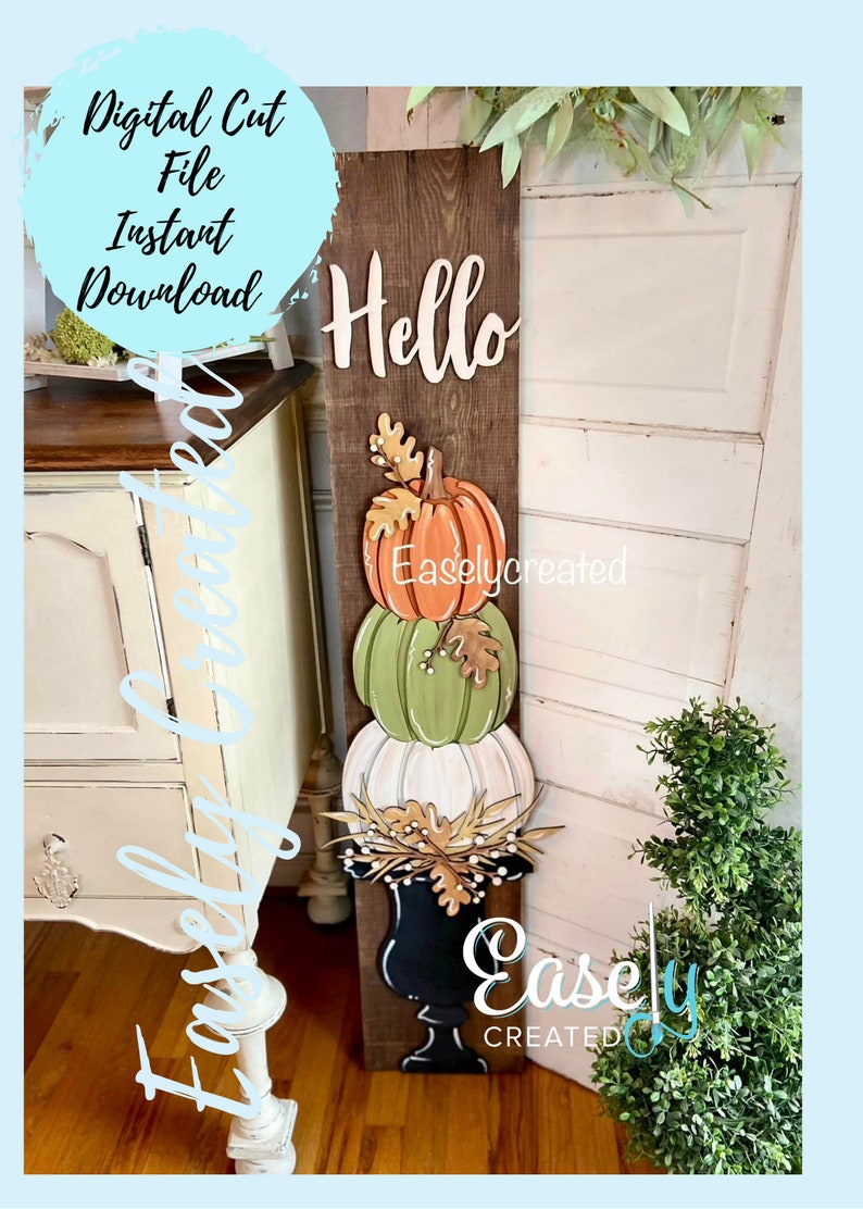May include: A wooden sign with the word "Hello" painted in white. Three stacked pumpkins in orange, green, and white are attached to the sign. The pumpkins are decorated with leaves and berries. The sign is leaning against a white door.