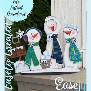 May include: Three wooden snowman figures with painted details, including scarves, hats, and snowballs. The snowmen are standing on a wooden base with the text "Snowballs for Sale" on a sign.