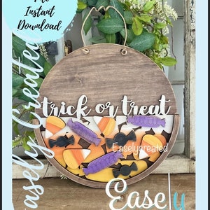 Pu&ograve; includere: Un cartello rotondo in legno con il testo "trick or treat" in lettere bianche. Il cartello &egrave; decorato con mais caramellato, barrette di cioccolato e lecca-lecca in arancione, giallo, viola e nero. Il cartello &egrave; appeso a una corda e ha uno sfondo marrone.