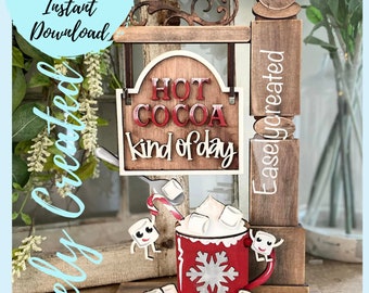 Könnte beinhalten: Ein Holzschild mit dem Text "HOT COCOA kind of day" hängt an einem Holzständer. Eine rote Tasse mit einem Schneeflockenmuster ist mit weißen Marshmallows und einem Zuckerrohr gefüllt. Zwei kleine Marshmallow-Figuren befinden sich auf beiden Seiten der Tasse.