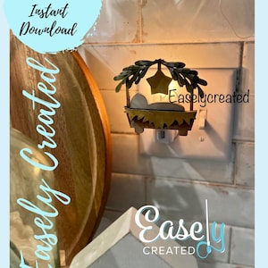 May include: A metal nativity scene nightlight plugged into an outlet. The scene features a manger with a baby Jesus inside, surrounded by greenery and a star. The nightlight is lit and glowing.