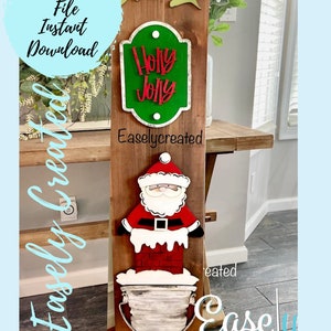 Peut inclure: Une pancarte en bois avec une figurine de Père Noël, un seau et une pancarte verte qui dit "Holly Jolly". La pancarte est décorée de feuilles vertes et les mots "Easlycreated" sont imprimés sur la pancarte.